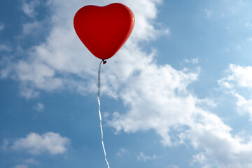 Fototapeta na wymiar red heart-shaped balloon on blue sky background with clouds