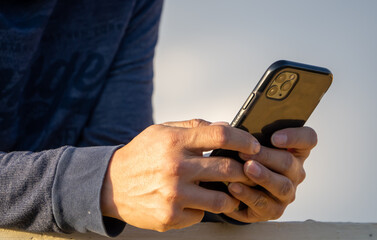close up de las manos de un hombre sosteniendo su teléfono celular, realizando negocios desde la distancia a través de la tecnología - obrazy, fototapety, plakaty