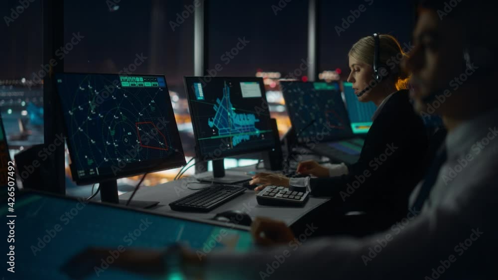 Wall mural Female Air Traffic Controller with Headset Talk on a Call in Airport Tower at Night. Office Room is Full of Desktop Computer Displays with Navigation Screens, Airplane Flight Radar Data for the Team.