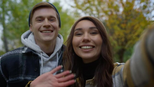 Cheerful young couple waving hands on selfie video on smartphone outdoors. 