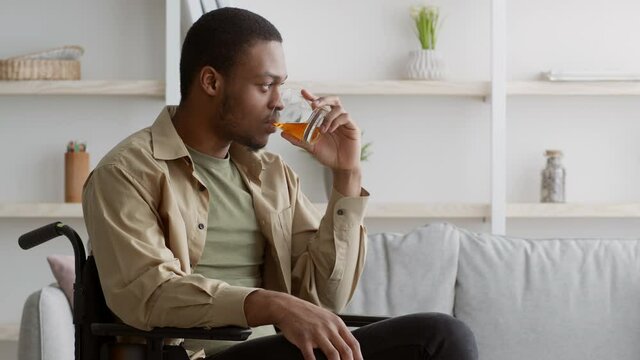 Depressed handicapped black man drinking whiskey sitting in wheelchair indoor