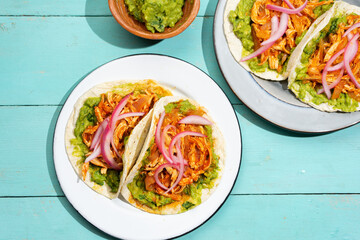 Chicken tinga tacos with guacamole and onion on turquoise background. Mexican food