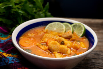 Fish soup with vegetables on wooden background. Mexican food