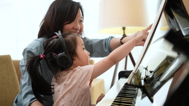 Medium close up shot of Asian mother and daughter practice piano together with happy and fun,  Music class learning at home.