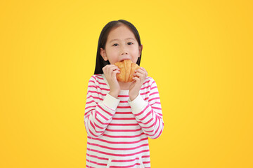 Asian little child girl eating croissant isolated on yellow background with clipping path