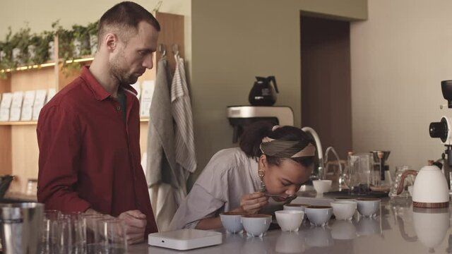 Medium shot of two professional female and baristas tasting different types of coffee in cup tasters in bar. Coffee degustation