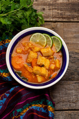 Fish soup with vegetables on wooden background. Mexican food