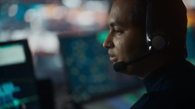 Close Up Portrait of Male Air Traffic Controller with Headset Talk on a Call in Airport Tower. Office Room is Full of Desktop Computer Displays with Navigation Screens, Airplane Flight Radar Data.