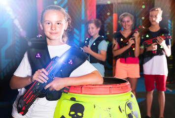 Portrait of girl standing with laser gun on dark lasertag arena on background with his team..