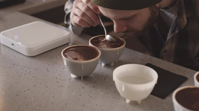 Close up of professional male barista tasting different types of coffee in cup tasters in cafe. Coffee degustation