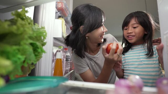asian mother and her daughter having snack time together in the kitchen open the fridge shoot from inside