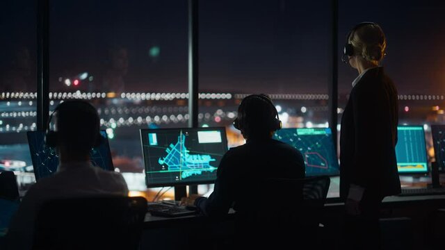 Female and Male Air Traffic Controllers with Headsets Talk in Airport Tower at Night. Office Room Full of Desktop Computer Displays with Navigation Screens, Airplane Flight Radar Data for Controllers.