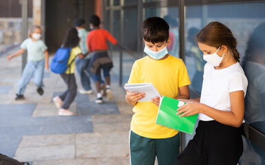 Portrait of primary school girl and boy wearing protective face masks talking outside before...