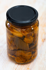 Closed glass jar with pickled red pine mushroom (lactarius deliciosus) on wooden table