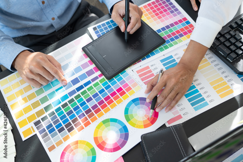 Poster graphic designer or creative working together coloring using graphics tablet and a stylus at desk wi