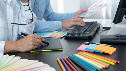 Graphic designer or creative working together coloring using graphics tablet and a stylus at desk...