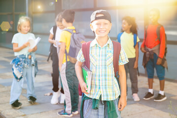 Smiling boy standing after classes near school with fellow classmates on background
