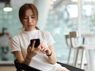 Half-length portrait of female using smartphone while sitting on the armchair in library