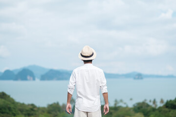 Fototapeta na wymiar Happy traveler man in white shirt enjoy Beautiful view, alone Tourist with hat standing and relaxing over ocean. travel, summer and vacation concept