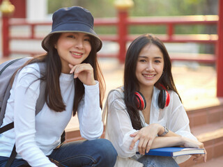 Portraits of two friendly female college students smiling to camera while relaxed sitting on staircase