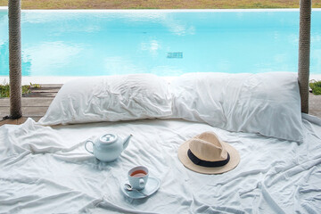 Traveler hat, hot tea cup and teapot on white bed against Beautiful ocean view background, Tourists...