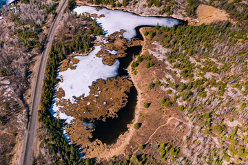 A still frozen lake sits beside a Canadian railway.  Spring has come and the ice is beginning to melt.