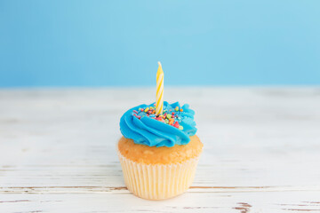 Birthday greeting concept. Yellow candle on muffin, cupcake. Blue background