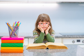 A girl with down syndrome enthusiastically reads a book that lies in front of her on the table. Affordable education for everyone concept