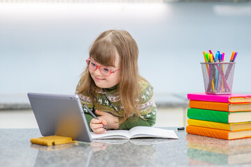 A girl with down syndrome is engaged in lessons using a tablet. Child down smiling while looking at the computer during class. Accessibility of education for children with disabilities