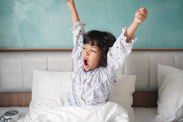 Asian kid yawning after waking up and stretching arms on the bed in the morning.