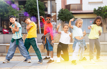 International group of modern tweenagers performing street dance choreography outdoors in summer.