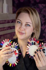 Portrait of a woman with varnish palettes. Close-up portrait of a manicure master in the workplace with palettes of multi-colored varnish. Manicurist in a black jacket at the workplace. 