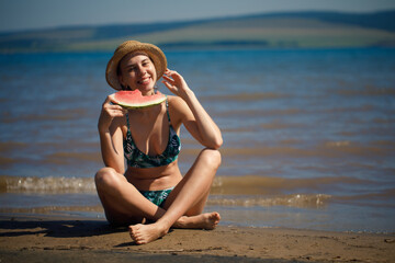 Fototapeta premium Portrait of smiling woman relaxing holding and eating a slice of watermelon on the tropical beach