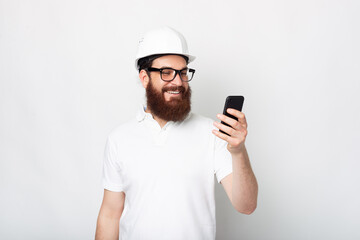 Photo of cheerful engineer man using smartphone and wearing hard hat
