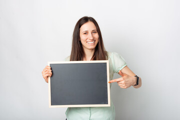 Fototapeta premium Portrait of smiling young beautiful woman pointing at blank black chalkboard