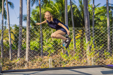 Young woman on a soft board for a trampoline jumping on an outdoor trampoline, against the backdrop of palm trees. The trampoline board is like a wakeboard, skateboard or snowboard trainer to hone