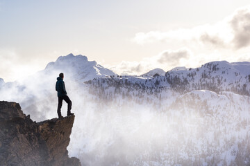 Fantasy Adventure Composite with a Man on top of a Mountain Cliff with Dramatic Landscape in Background during Sunset or Sunrise. Landscape from British Columbia, Canada.