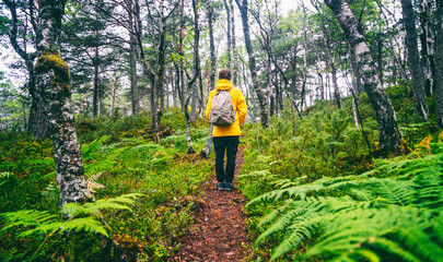 Woman traveler in yellow jacket with backpack standing in green forest © olezzo