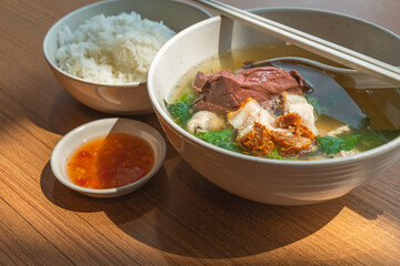 Close up Asian meal, a bowl of pig's blood soup and pork with steam white rice and spicy-sour sauce, natural light on table. Pig's blood soup and pork is called Tom Leard Moo in the Thailand language.
