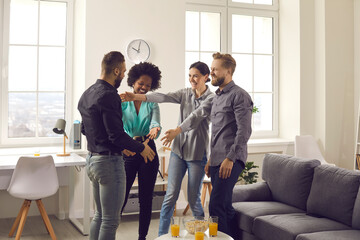 Male and female friends welcoming young guy at cozy party at home. Group of happy people excited to...