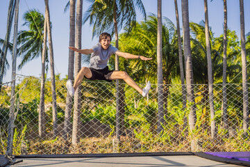 Happy man jumping on an outdoor trampoline, against the backdrop of palm trees