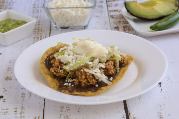Traditional Mexican food. Picadillo toast with guacamole, sour cream, lettuce and cheese, accompanied by avocado slices and jalapeño peppers.