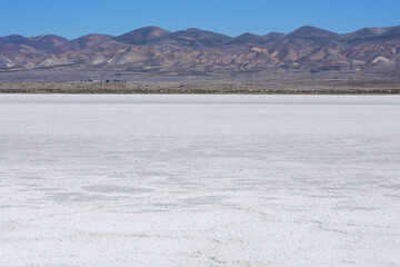 White salt flats of dry Soda Lake at Carrizo Plain National Monument with power line near lake shore. Temblor Range mountains on horizon on hot sunny day.