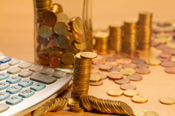 Pile of coins on a table with a lot of different coins around it and a calculator on a wooden table. Save money concept banner