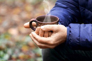 Elderly woman holding a cup of hot tea in the woods in nature. Outdoor recreation