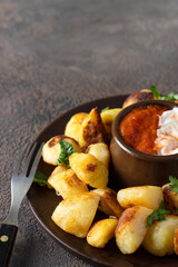 Spanish tapa Patata bravas, typical potatoes snack served with different sauces on black background