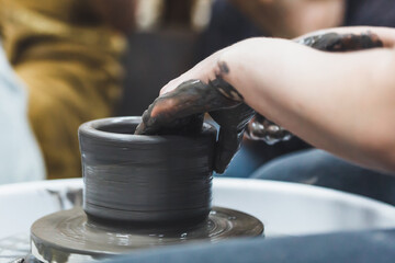 Working with a potter's wheel with gray clay. The hands of a girl potter.