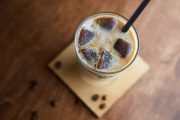 Ice coffee in a tall glass with cream poured over and coffee beans. Cold summer drink on a cafe table