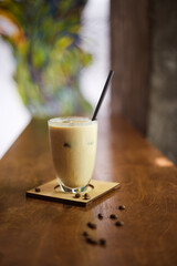 Ice coffee in a tall glass with cream poured over and coffee beans. Cold summer drink on a cafe table