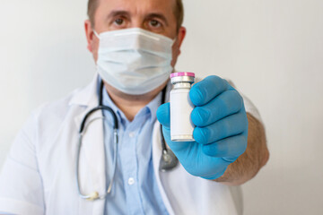 A male doctor, wearing a protective mask with a stethoscope, holds a bottle of vaccine in his hand, copyspace